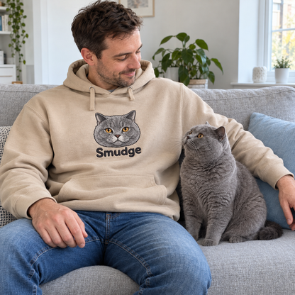 Man on a sofa with his grey British Shorthair Smudge, wearing a Desert Dust hoodie embroidered with Smudge